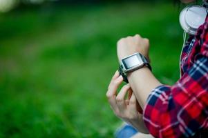 la ragazza guarda l'orologio in mano, guarda l'ora con un orologio nero, indossa una maglietta rossa e uno sfondo verde. e c'è uno spazio di copia. foto