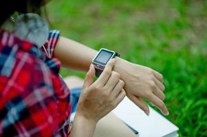 la ragazza guarda l'orologio in mano, guarda l'ora con un orologio nero, indossa una maglietta rossa e uno sfondo verde. e c'è uno spazio di copia. foto