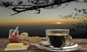 caffè nero in vetro trasparente e pane fatto in casa sul macellaio per il concetto di colazione su un tavolo di legno. sfocatura dello sfondo vista mountian e alba. rendering 3D. foto