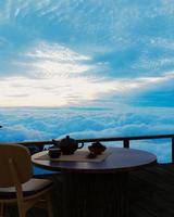 servizio da tè in ceramica e foglie di tè secco su un tavolo e una sedia di legno sul balcone o sulla terrazza in legno. montagna con mare mattutino di nebbia e sole. tè caldo nell'atmosfera di montagna. rendering 3D foto