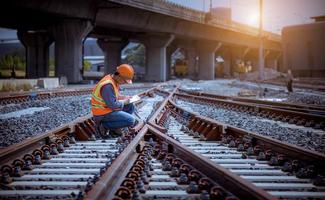 ingegnere ferroviario in fase di controllo del processo di costruzione test del treno e controllo dei lavori ferroviari sulla stazione ferroviaria con comunicazione radio. ingegnere che indossa l'uniforme di sicurezza e il casco di sicurezza sul lavoro. foto