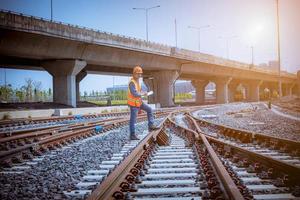 ingegnere ferroviario in fase di controllo del processo di costruzione test del treno e controllo dei lavori ferroviari sulla stazione ferroviaria con comunicazione radio. ingegnere che indossa l'uniforme di sicurezza e il casco di sicurezza sul lavoro. foto