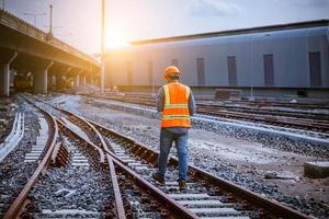 ingegnere ferroviario in fase di controllo del processo di costruzione test del treno e controllo dei lavori ferroviari sulla stazione ferroviaria con comunicazione radio. ingegnere che indossa l'uniforme di sicurezza e il casco di sicurezza sul lavoro. foto