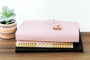 area di lavoro a tema femminile e femminile con organizer rosa, taccuino ad anello e album da disegno con copertina nera sul piano del tavolo in legno. foto
