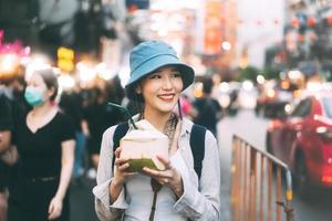 giovane adulto asiatico foodie donna zaino viaggiatore mangiare succo di cocco al cibo di strada della città cinese. foto