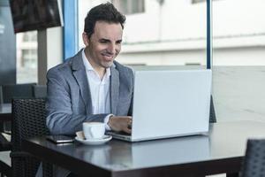 uomo d'affari felice che lavora con il computer portatile in un caffè moderno foto