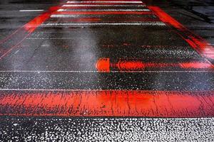 strada asfaltata bagnata con strisce pedonali rosse e bianche. foto