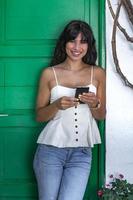 donna etnica felice che utilizza smartphone vicino alla porta foto