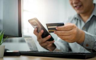 un uomo in possesso di carta di credito e che utilizza lo smartphone per il pagamento online per l'acquisto dopo l'ordine di prodotti tramite Internet. il concetto di tecnologia per l'e-commerce foto