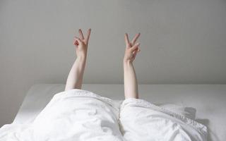 donna che mostra la pace o il segno della mano v mentre giaceva in un letto accogliente e si nascondeva sotto le coperte foto