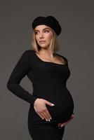 elegante bella donna incinta in un vestito nero tiene le mani sullo stomaco. foto