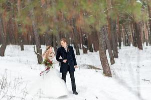 gli allegri sposi in pullover lavorati a maglia beige stanno camminando nella foresta innevata. matrimonio invernale foto