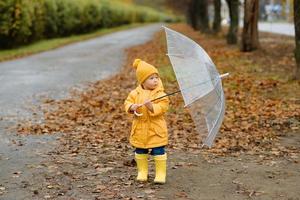 una bambina cammina con un ombrello con stivali di gomma gialli e un impermeabile impermeabile. passeggiata autunnale. foto
