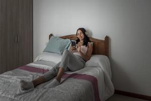donna contenta che ascolta musica e naviga sullo smartphone sul letto foto