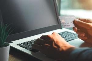 mano dell'uomo d'affari che tiene la carta di credito con l'utilizzo del laptop per lo shopping online mentre si effettuano gli ordini a casa. business, stile di vita, tecnologia, e-commerce, digital banking e concetto di pagamento online. foto