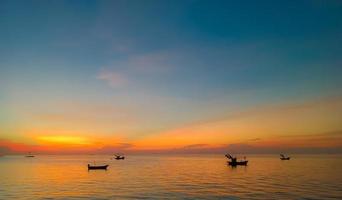 cielo e mare al tramonto, barche locali che galleggiano in mezzo al mare, cielo arancione e blu che riflette il mare, dando una sensazione di calma. foto