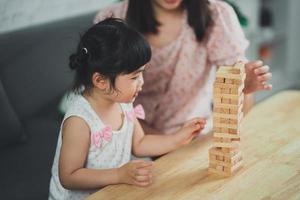 concetto di giochi di jenga. figlia e madre asiatiche sorridono felici e ridono giocando a giochi di legno jenga seduti sul divano in soggiorno a casa, madre e figlia attività familiari che giocano a giochi felici foto