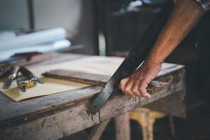 anziano falegname anziano che usa la sega che lavora su artigianato in legno in officina per produrre materiale da costruzione o mobili in legno. foto