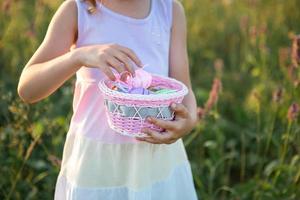 ragazza carina e divertente con uova di Pasqua dipinte in primavera in natura in un campo con luce solare dorata e fiori. vacanze di pasqua, coniglietto pasquale con le orecchie, uova colorate in un cestino. stile di vita foto