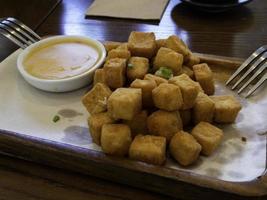 tofu fritto su un piatto di legno. ciotolina con forchetta cucchiaio per salsa foto