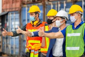 concetto di lavoro di squadra di successo, ingegnere di uomini d'affari e team di lavoratori che indossano una maschera protettiva contro il coronavirus con i pollici in su come segno di successo foto