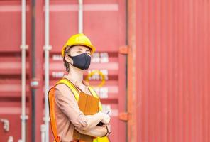 ingegnere con elmetto protettivo e giubbotto di sicurezza con lista di controllo per appunti e radio ricetrasmittente, donna che indossa una maschera protettiva contro il coronavirus al carico dei container foto