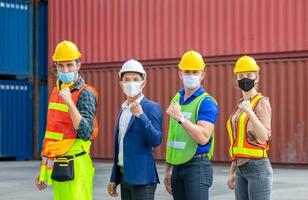 team di ingegneri e lavoratori che indossano una maschera protettiva contro il coronavirus, celebrazione del team di uomini d'affari felici con sfondo sfocato dei contenitori di carico foto