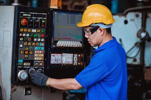 ingegneria industriale che indossa un controllo uniforme di sicurezza che opera una rettificatrice per tornio controllata da computer che lavora in una fabbrica industriale. foto