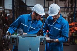 ingegneria industriale che indossa un controllo uniforme di sicurezza che opera una rettificatrice per tornio controllata da computer che lavora in una fabbrica industriale. foto