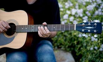 immagine di un chitarrista, un giovane che suona una chitarra mentre è seduto in un giardino naturale, concetto musicale foto