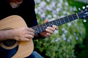 immagine di un chitarrista, un giovane che suona una chitarra mentre è seduto in un giardino naturale, concetto musicale foto