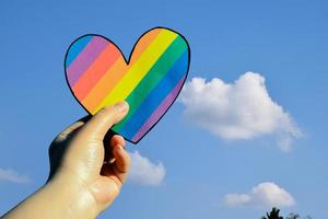 due cuori fatti di carta color arcobaleno tengono nelle mani della persona lgbt, concetto per le celebrazioni delle comunità lgbtq nel mese dell'orgoglio in tutto il mondo foto