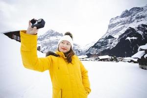 grindelwald svizzera cima d'europa, donna asiatica che indossa un cappotto giallo. usa lo smartphone scatta una foto montagna di neve nella sua vacanza in montagna, viaggio inverno nevoso sul monte a grindelwald.