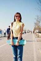 giovane ragazza adolescente con piccolo skateboard, penny board, indossare su t-shirt gialla, jeans e occhiali da sole. foto