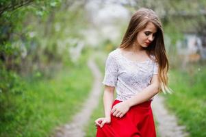 ritratto di bella ragazza con labbra rosse al giardino di fiori primaverili, indossare su abito rosso e camicetta bianca. foto