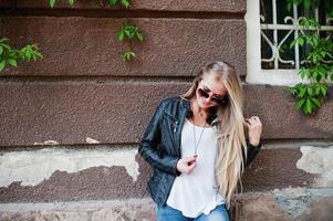 elegante donna bionda indossare jeans e giacca poste in strada contro il muro. ritratto di modello urbano di moda. foto