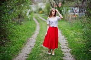 ritratto di bella ragazza con labbra rosse al giardino di fiori primaverili, indossare su abito rosso e camicetta bianca. foto