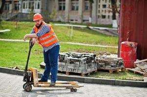 barba brutale lavoratore uomo vestito operaio edile in sicurezza casco arancione con transpallet. foto