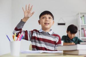 studente asiatico intelligente e attivo che alza la mano durante la lezione di classe per rispondere alla domanda foto