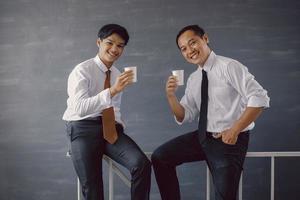 due uomini d'affari asiatici in camicia bianca e cravatta sorridenti mentre offrono caffè alla fotocamera foto