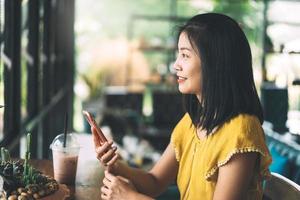 donna asiatica felice adulta che utilizza il telefono cellulare al bar al coperto il giorno. foto