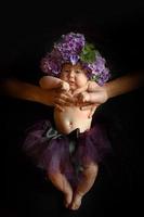 le mani del padre tengono in testa una figlia piccola con fiori di ortensia. girato su sfondo nero. foto