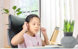 bambina allegra sorridente e mentre utilizza laptop e auricolare wireless per videochiamate, istruzione e concetto di apprendimento a distanza foto