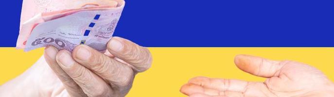 mano che tiene soldi sulla bandiera ucraina, idea per aiutare il popolo ucraino foto