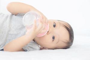 primo piano di adorabile bambino che beve latte da una bottiglia e guarda la fotocamera foto