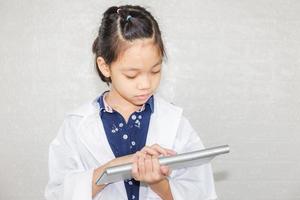 concetto di carriera da sogno, dottoressa bambina che digita sulla tastiera del computer wireless, ritratto di bambino felice in camice medico con sfondo sfocato foto