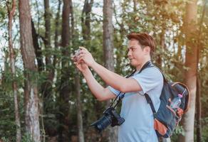 un turista maschio che porta una borsetta, una bottiglia d'acqua e una macchina fotografica cammina attraverso la foresta. foto
