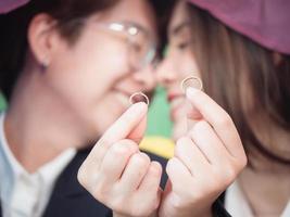 primo piano di fedi nuziali. felice coppia lesbica mostra anelli di fidanzamento in mano su sfondo bandiera arcobaleno lgbt a casa. concetto di proposta di matrimonio nella coppia gay foto