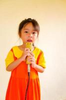 adorabile bambina indossa vestito giallo-arancio vestito gokowa o mugunghwa e tiene il microfono dorato che canta musica. ragazze e abiti alla moda per adolescenti. foto