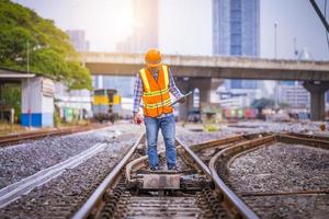 ingegnere ferroviario in fase di controllo del processo di costruzione test del treno e controllo dei lavori ferroviari sulla stazione ferroviaria con comunicazione radio. ingegnere che indossa l'uniforme di sicurezza e il casco di sicurezza sul lavoro. foto